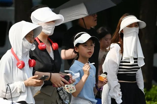 People wear head coverings during a heatwave in Beijing on June 23, 2023. China issued its highest-level heat alert for northern parts of the country on June 23 as the capital baked in temperatures hovering around 40 degrees Celsius (104 Fahrenheit). (Photo by Greg Baker/AFP Photo)