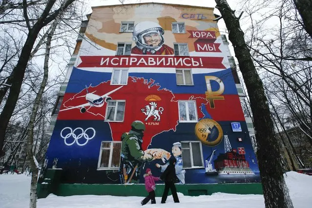 A woman and child walk past a residential building decorated with graffiti reading “Yura, we have improved!” and depicting Soviet cosmonaut Yuri Gagarin, a map of Crimea, a Sukhoi Superjet 100, a 2014 Sochi Olympic medal, a Russian rouble sign and an oil platform, in Moscow, February 5, 2015. (Photo by Maxim Zmeyev/Reuters)