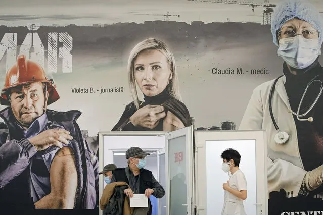 A man holds his vaccination certificate as he walks under large posters advertising the COVID-19 vaccination campaign at a vaccination center that offers both AstraZeneca and Pfizer vaccines in Bucharest, Romania, Tuesday, March 23, 2021. AstraZeneca's repeated missteps in reporting vaccine data coupled with a blood clot scare could do lasting damage to the credibility of a shot that is the linchpin in the global strategy to stop the coronavirus pandemic, potentially even undermining vaccine confidence more broadly, experts say. (Photo by Vadim Ghirda/AP Photo)