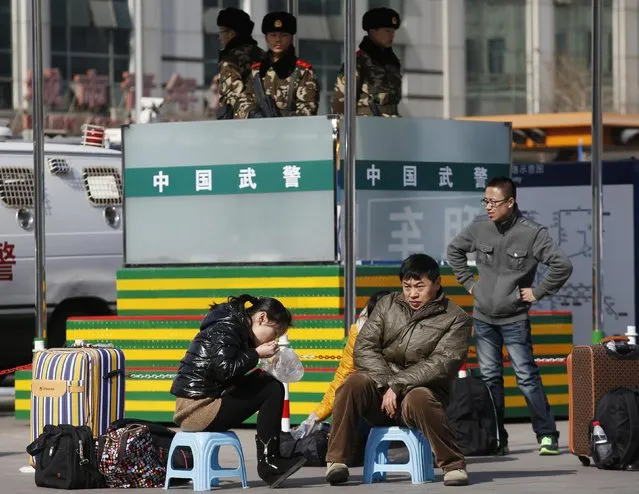 People sit on stools as they wait for their trains in front of paramilitary policemen at a railway station in Beijing February 16, 2015. (Photo by Kim Kyung-Hoon/Reuters)