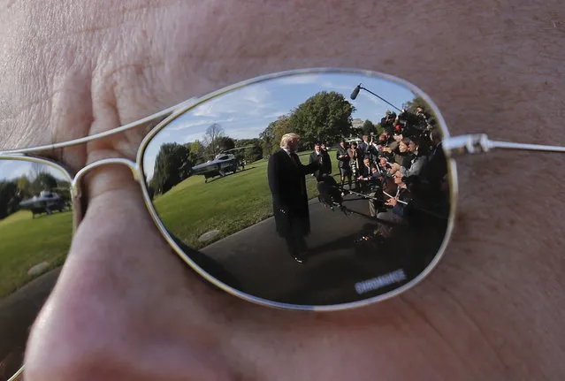 President Donald Trump, seen reflected in the sunglasses of a Secret Service agent, as Trump stops to speak to members of the media before walking across the South Lawn of the White House in Washington, Monday, October 22, 2018, to board Marine One helicopter for a short trip to Andrews Air Force Base, Md., en route to Houston. (Photo by Pablo Martinez Monsivais/AP Photo)