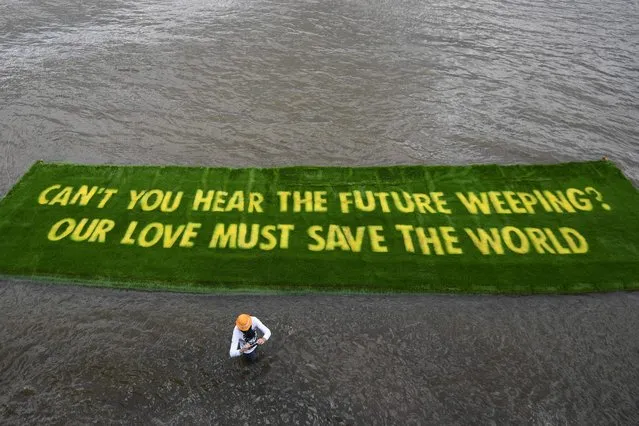 A giant banner declaring an environmental message, which is grown on a carpet of living grass and tells governments to Act Now in the lead-up to COP26, floats on the river Thames in central London on June 25, 2021, having been placed on the water by Extinction Rebellion climate activists. (Photo by Daniel Leal-Olivas/AFP Photo)