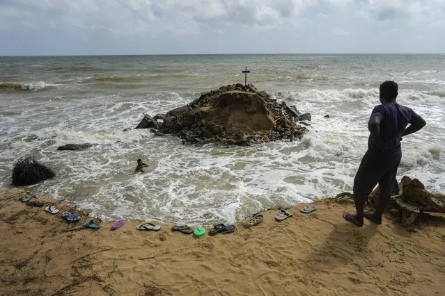 A man watches Nuwan Fernando, left, in the water, who wades in the tide to collect stones washed out from his land due to coastal erosion in Iranawila, Sri Lanka, Monday, June 19, 2023. “I don't know what will happen in the future but I still keep my faith”, Fernando said, one of a few in Iranawila whose house remains intactEranga Jayawardena