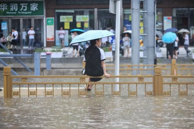 This photo taken on July 20, 2021 shows a woman sitting on a fence on a flooded street following heavy rains in Zhengzhou in China's central Henan province. (Photo by AFP Photo/China Stringer Network)