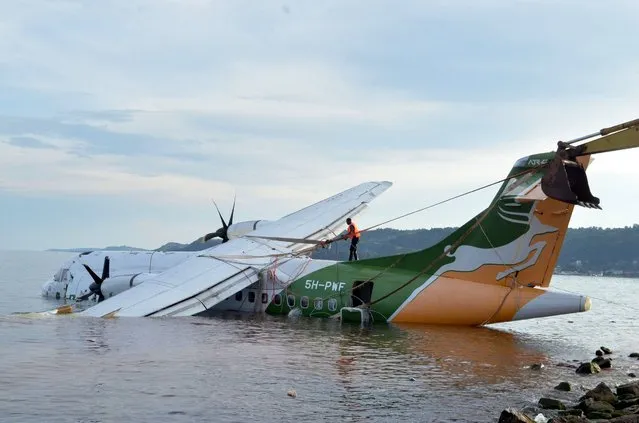 A rescuer ties a winch to pull out the crashed Precision Air flight that was carrying 43 people and plunged into Lake Victoria as it attempted to land in the lakeside town of Bukoba, Tanzania on November 6, 2022. Three people died when a plane carrying dozens of passengers plunged into Lake Victoria in Tanzania on November 6, 2022, as it approached the northwestern city of Bukoba, the fire and rescue service said. Rescuers have pulled 26 survivors to safety after the Precision Air plane crashed due to bad weather, with 43 people, including 39 passengers, aboard flight PW 494 from the financial capital Dar es Salaam to the lakeside city, according to regional authorities. (Photo by Sitide Protase/AFP Photo)