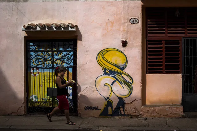 A woman passes by a closed art store decorated by a mural in Havana, Cuba, Wednesday, December 5, 2018. After weeks of public debates and overlapping complaints from artists and intellectuals about a decree that increased control for artists and promoters, Cuban authorities are about to publicize complementary rules that limit the power of cultural inspectors and limit official action about creation. (Photo by Desmond Boylan/AP Photo)