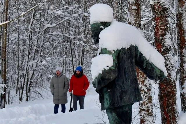 People walk past a snow-covered bronze monument depicting Soviet state founder Vladimir Lenin and created by Soviet sculptor Matvey Kharlamov in a park of a museum complex in Razliv, outside Saint Petersburg, on January 21, 2024. On January 21 Russia marks the 100th anniversary of the death of Vladimir Illitch Lenin, who was placed in the mausoleum in Moscow, despite his wish to be buried near his mother at the Volkovo cemetery in Saint Petersburg. (Photo by Olga Maltseva/AFP Photo)
