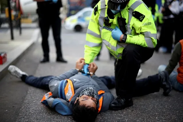 A police officer detains an Insulate Britain activist lying on the road during a protest in London, Britain on October 25, 2021. (Photo by Henry Nicholls/Reuters)