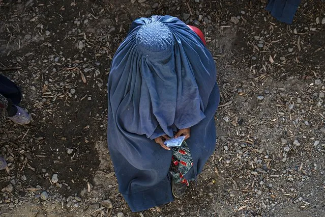 An Afghan burqa-clad woman waits to receive cash money being distributed as an aid by the World Food Programme (WFP) organisation in Pul-i-Alam, the provincial capital of Logar Province on January 7, 2024. (Photo by Wakil Kohsar/AFP Photo)