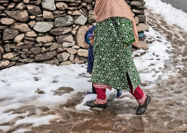 A woman walks with a child on a snow covered road to get him polio drops at a government health centre in Srinagar, Indian controlled Kashmir, Sunday, March 3, 2024. India eradicated polio more than a decade ago after successfully implementing a polio immunization programme adopted in 1995. (Photo by Mukhtar Khan/AP Photo)