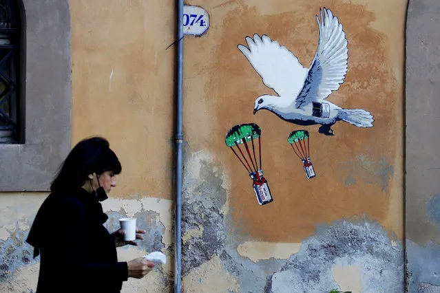 A woman walks past a mural depicting a white dove parachuting COVID-19 vaccine vials, posted near the Italian Health Ministry Headquarters in Rome, April 4, 2021. The pandemic is again roaring across parts of Western Europe, a prosperous region with relatively high vaccination rates and good health care systems but where lockdown measures to rein in the virus are largely a thing of the past. Italy, an early victim of the pandemic, has a high vaccination rate, but is also seeing numbers edge higher, which experts believe is due to vaccine efficacy wearing off. (Photo by Gregorio Borgia/AP Photo)