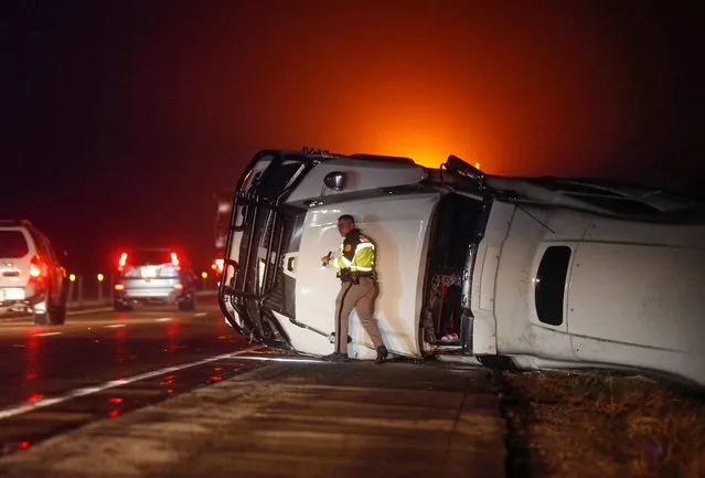 An Iowa State Patrol trooper works the scene of an overturned semi truck along the westbound shoulder of Interstate 80 near Anita, Iowa, on Wednesday, December 15, 2021, after a band of intense weather crossed through the area. A powerful storm system is blowing through the Great Plains and Midwest, combining with unusually warm temperatures to close highways and prompt numerous tornado warnings. (Photo by Bryon Houlgrave/The Des Moines Register via AP Photo)