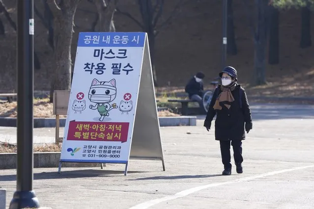 A visitor wearing a face mask as a precaution against the coronavirus, walks near a banner at a park in Goyang, South Korea, Saturday, December 4, 2021. South Korea again broke its daily records for coronavirus infections and deaths and confirmed three more cases of the new omicron variant as officials scramble to tighten social distancing and border controls. The banner reads “Mandatory mask wearing”. (Photo by Lee Jin-man/AP Photo)