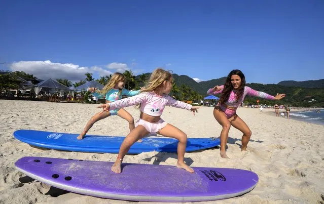 Rayana Tanimoto teaches her five-year-old twin daughters Eloa, left, and Ayla, how to surf, at Maresias beach, in Sao Sebastiao, Brazil, Saturday, November 27, 2021. Tanimoto, caught the surfing bug from her father. Together, they opened a small hotel on Maresias beach so she could raise her daughters, make a living and get in the water as often as possible. (Photo by Andre Penner/AP Photo)