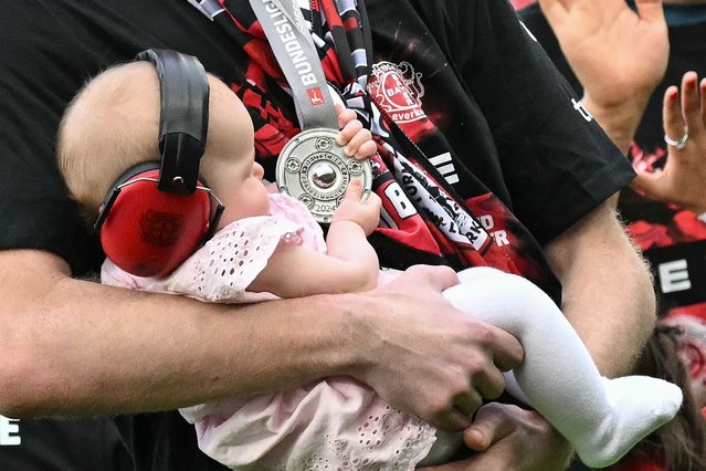 Bayer Leverkusen's Finnish goalkeeper #01 Lukas Hradecky holds his baby wearing ear protection as it checks out his winners medal after the German first division Bundesliga football match between Bayer 04 Leverkusen and FC Augsburg in Leverkusen, western Germany on May 18, 2024. (Photo by Ina Fassbender/AFP Photo)
