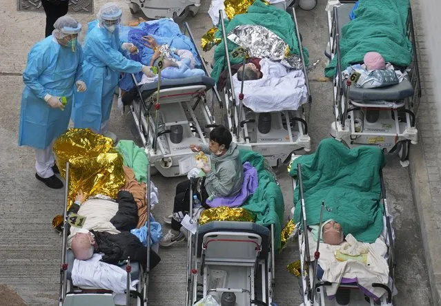Patients lie on hospital beds as they wait at a temporary holding area outside Caritas Medical Centre in Hong Kong Wednesday, February 16, 2022. There was visible evidence that Hong Kong hospitals were becoming overwhelmed by the latest COVID surge, with patients on stretchers and in tents being seen to by medical personnel on Wednesday outside the Caritas hospital. (Photo by Vincent Yu/AP Photo)
