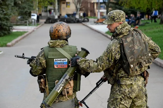 Armed men wearing military fatigues show a sticker with text reading “Donetsk don't listen to Kiev” during a pro-Russian rally, in the eastern Ukrainian city of Slavyansk on April 19, 2014. Pro-Russian rebels kept their grip on seized government buildings in Ukraine today, a day after Kiev struck a deal with Russia and the West aimed at easing the crisis in the ex-Soviet republic. (Photo by Kirill Kudryavtsev/AFP Photo)