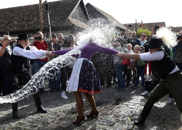 A woman dressed in traditional clothes reacts as men throw water at her during a traditional Easter celebration in Holloko, Hungary, on April 1, 2024. (Photo by Bernadett Szabo/Reuters)