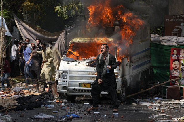 Supporters of former Prime Minister Imran Khan throw stones toward police next a burning vehicle during clashes, in Lahore, Pakistan, Wednesday, March 15, 2023. Supporters of Khan threw bricks at police who fought back with clubs and tear gas for a second day Wednesday after officers tried to arrest the ousted premier for failing to appear in court on graft charges.(Photo by K.M. Chaudary/AP Photo)