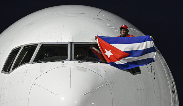 Cuban wrestler Mijain Lopez Nunez, a five-time Olympic champion, waves a Cuban flag from the pilot's window of a plane as he arrives at Jose Marti airport in Havana, Cuba, Monday, August 12, 2024. (Photo by Adalberto Roque/Pool Photo via AP Photo)