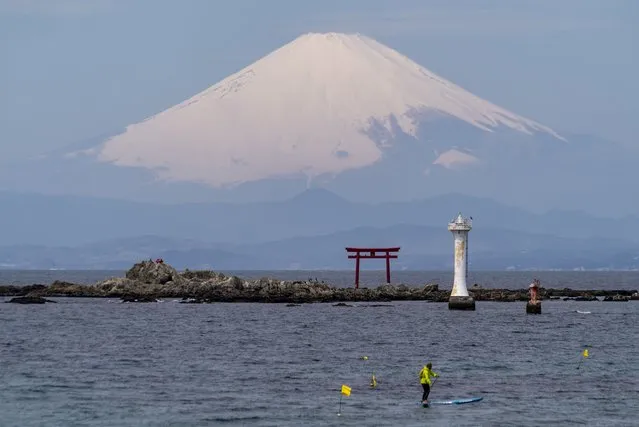 With Mount Fuji in the background, a standup paddleboarder cruises near a Torii gate, an entrance gate to a Shinto shrine, in Sagami Bay Wednesday, April 6, 2022, in Zushi, south of Tokyo. (Photo by Kiichiro Sato/AP Photo)