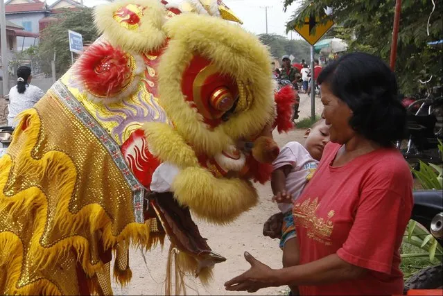 A Cambodian villager, right,  holds her grandchild as she offers some money during a performance of a local lion dance called “Mong Say” during Buddhist Lent in Prek Takov village, Kandal province, northeast of Phnom Penh, Cambodia, Monday, July 27, 2015. (Photo by Heng Sinith/AP Photo)