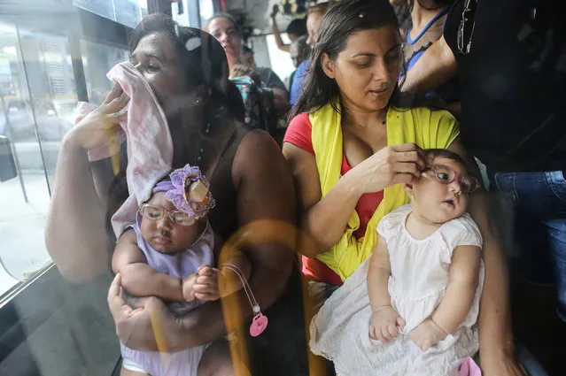 Mothers Jusikelly (R) and Inabela hold their daughters Luhandra (R) and Graziella, both born with microcephaly, as they wear their new glasses on a bus ride after a clinic visit on June 2, 2016 in Recife, Brazil. Microcephaly is a birth defect linked to the Zika virus where infants are born with abnormally small heads. Some of these infants are also suffering from vision problems in Brazil. Mothers often must ride many hours on buses to take their children for medical visits. (Photo by Mario Tama/Getty Images)