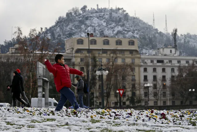 A boy winds up with a snowball in hand in a park in Santiago, Chile, Saturday, July 15, 2017. Record cold temperatures and an unusual snowfall hit Chile's capital Saturday. Normal temperatures are expected to return midweek. (Photo by Esteban Felix/AP Photo)
