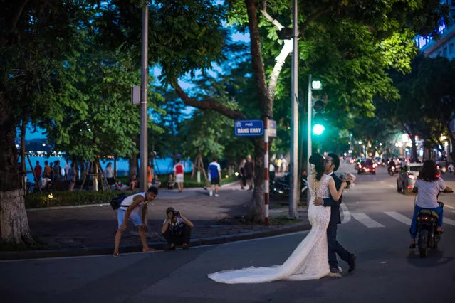 In this photograph taken on July 19, 2017, a bride and groom get their photo taken by a portrait photographer in the streets of downtown Hanoi. (Photo by Roberto Schmidt/AFP Photo)