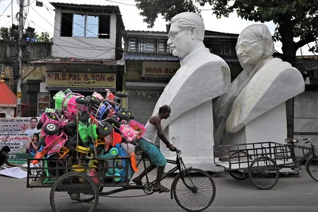 A man rides a rickshaw loaded with tricycles past the statues of Mahatma Gandhi (R) and Bangladesh's founder Sheikh Mujibur Rahman before their installation near a railway station as part of the golden jubilee celebration Bangladesh's independence, in Kolkata on June 28, 2022. (Photo by Dibyangshu Sarkar/AFP Photo)