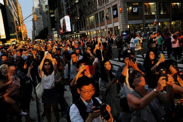 People stand in the middle of 42nd Street in Times Square to take pictures as the sun sets over Manhattan aligned exactly with the streets in a phenomenon known as “Manhattanhenge”, in New York City, U.S., July 11, 2016. (Photo by Mark Kauzlarich/Reuters)