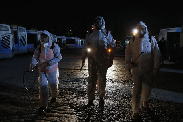 Workers wearing protective suits walk at a bus depot before they spray disinfectant inside the vehicles in Athens, Saturday, March 14, 2020. Greece has announced new sweeping closures Friday, closing all shopping malls, cafes, bars and restaurants, except those that provide only take-aways or deliveries. All museums, ancient sites, libraries and beauty salons will also shut down. For most people, the new coronavirus causes only mild or moderate symptoms, such as fever and cough. For some, especially older adults and people with existing health problems, it can cause more severe illness, including pneumonia. (Photo by Thanassis Stavrakis/AP Photo)