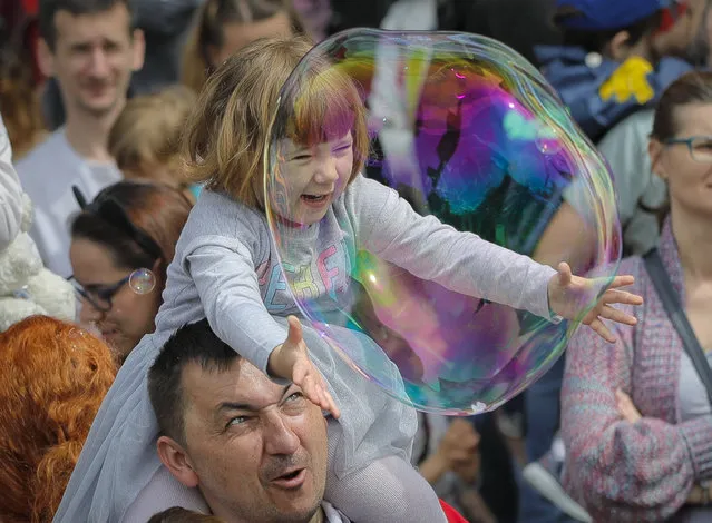 A child reaches for a soap bubble during the Global Bubble Parade in Bucharest, Romania, Sunday, May 5, 2019. Dozens took part in the Global Bubble Parade, an international event, held in 125 cities across 60 countries, according to the organizers, that brings together soap bubble fans. (Photo by Vadim Ghirda/AP Photo)