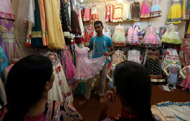 A shopkeeper shows a child's dress to customers ahead of Eid al-Fitr in Karachi, Pakistan July 4, 2016. (Photo by Akhtar Soomro/Reuters)