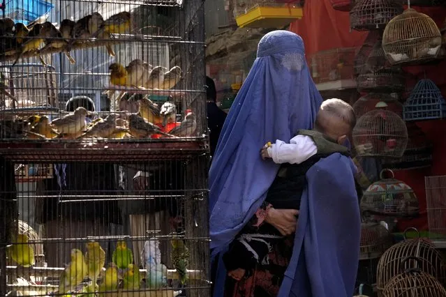 A woman wearing a burka walks through a bird market as she holds her child, in downtown Kabul, Afghanistan, Sunday, May 8, 2022. Afghanistan’s Taliban rulers on Saturday ordered all Afghan women to wear head-to-toe clothing in public – a sharp, hard-line pivot that confirmed the worst fears of rights activists and was bound to further complicate Taliban dealings with an already distrustful international community. (Photo by Ebrahim Noroozi/AP Photo)