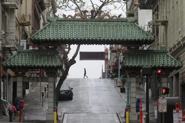 A pedestrian crosses Grant Street behind the Dragon Gate, an entrance to Chinatown in San Francisco, Saturday, April 4, 2020. (Photo by Jeff Chiu/AP Photo)