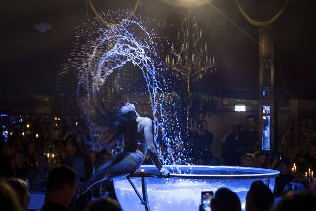 An artist performs her water acrobatics during the anniversary show to celebrate “20 years of Teatro” in Munich, Germany, Tuesday, November 21, 2023. The “Teatro” gastro tent celebrated its 20th birthday on Tuesday and its relaunch under new boss Michael Käfer. (Photo by Lennart Preiss/dpa via AP Photo)