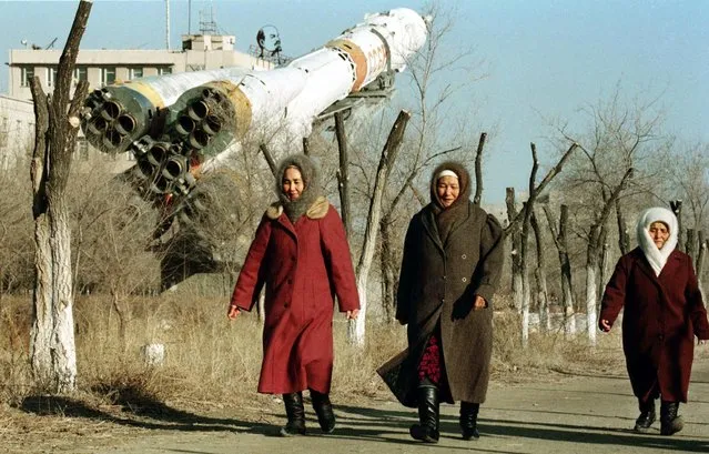 Three local women pass by a copy of Soyuz space craft with the name of former USSR country on it  and the portrait of Lenin in the backgrounds in the town of Baikonur, February 19, 1999. Tomorrow, February 20 the international Russian-Franco-Slovak space crew will take a flight to MIR space station on Soyuz-TM 29. (Photo by Alexander Nemenov/AFP Photo)
