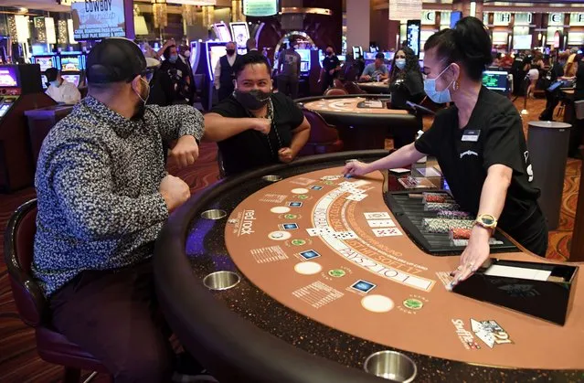 Evan Savar and Nabu Reyes, both of Nevada, bump elbows as they celebrate while playing blackjack with dealer Leah Prerost at the Red Rock Resort after the property opened for the first time since being closed on March 17 because of the coronavirus (COVID-19) pandemic, on June 4, 2020 in Las Vegas, Nevada. Hotel-casinos throughout the state are opening today as part of a phased reopening of the economy with social distancing guidelines and other restrictions in place. (Photo by Ethan Miller/Getty Images)