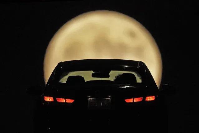 A motorist is silhouetted against the rising full Hunter's moon while driving, Sunday, October 9, 2022, in Shawnee, Kan. (Photo by Charlie Riedel/AP Photo)