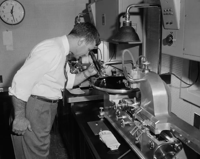 Robert Benezra uses a microscope to check the grooves as a machine makes a disc recording of a Voice of America broadcast, in Washington, D.C., December 14, 1954. (Photo by Bill Allen/AP Photo)