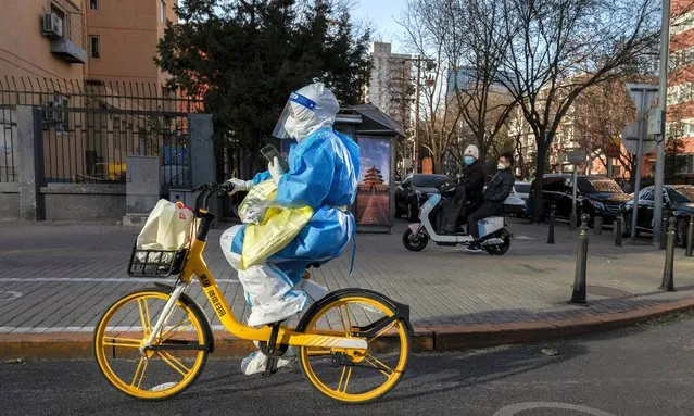 An epidemic control worker wears PPE to prevent the spread of COVID-19 as she rides a shared bike to give nucleic acid tests to people under health monitoring on November 30, 2022 in Beijing, China. (Photo by Kevin Frayer/Getty Images)