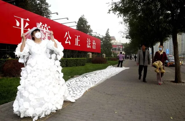 Chinese artist Kong Ning dressed in a 10-meter-long wedding gown made of 999 face masks poses on a street in smog in Beijing, China, 20 October 2014. Beijing's worsening air quality has spawned a new wave of anti-pollution based art projects created to increase awareness of the situation. (Photo by Imaginechina via AP Images)