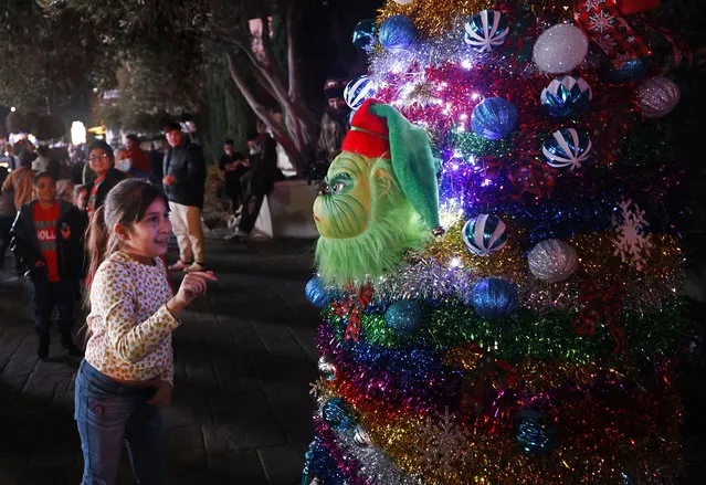 Celina Alas, 8, of Las Vegas, talks to the Grinch in a Christmas tree, Sunday, December 25, 2022, on the Las Vegas Strip. Performer David Lemesevic wears a Christmas tree costume and talks to the passers-by as the Grinch while videographer Igor Uzelac records prank videos for YouTube. (Photo by Chitose Suzuki/Las Vegas Review-Journal via AP Photo)