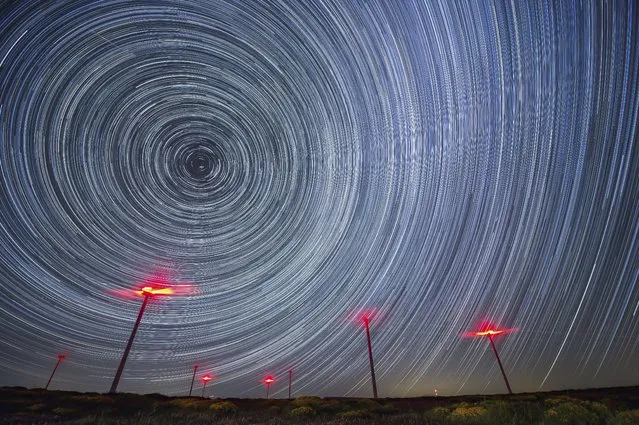 A rendered timelapse image shows circumpolar stars over some windmills taken from La Lora wasteland in Cantabria, Spain, early 31 May 2022. (Photo by Pedro Puente Hoyos/EPA/EFE)