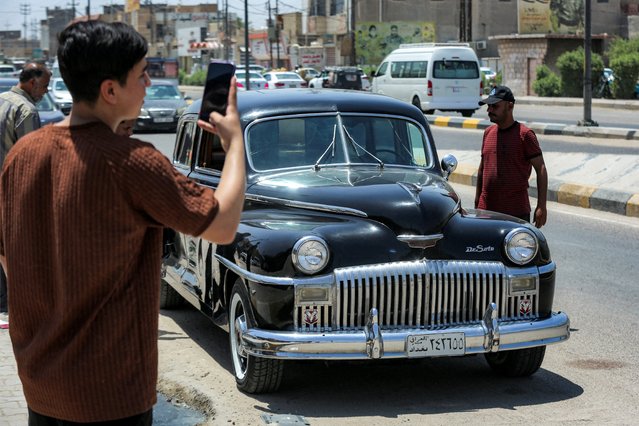 A youth takes a picture of a restored vintage 1940s-period DeSoto automobile parked along a street in Iraq's Alexandria (Iskandariya), south of Baghdad in Babylon province on May 27, 2025. (Photo by Karar Jabbar/AFP Photo)