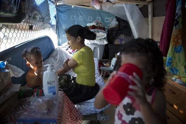 In this Tuesday, August 25, 2015 photo, Kifency Kinny, center, applies lotion to her arm and her 1-year-old son, J. Jee Suzuki while Kinny's niece, Keioleen Helly, drinks water in their makeshift tent at a homeless encampment in the Kakaako district of Honolulu. (Photo by Jae C. Hong/AP Photo)