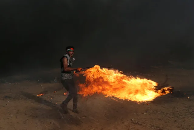 A demonstrator shouts as he carries a burning tire during a protest where Palestinians demand the right to return to their homeland, at the Israel-Gaza border, in the southern Gaza Strip May 18, 2018. (Photo by Ibraheem Abu Mustafa/Reuters)
