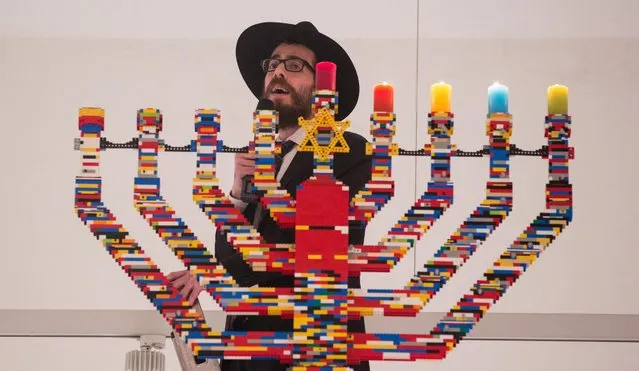 Rabbi Shmuel Havlin sings atop a ladder in front of Hanukkah candles made out of Lego blocks in the hall of the Joseph-Carlebach school in Hamburg, Germany, December 9, 2015. According to the Jewish educational center, students have built the world's highest Hanukkah Menorah from 30,000 Lego blocks. The newly built Hanukkah Menorah is 5.82 meters high. (Photo by Christian Charisius/dpa via AP Photo)