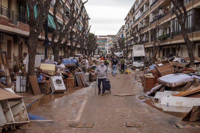 People walk through a street with piled furniture and rubbish on the sides, in an area affected by floods in Benetusser, Spain, on Monday, November 4, 2024. (Photo by Manu Fernandez/AP Photo)